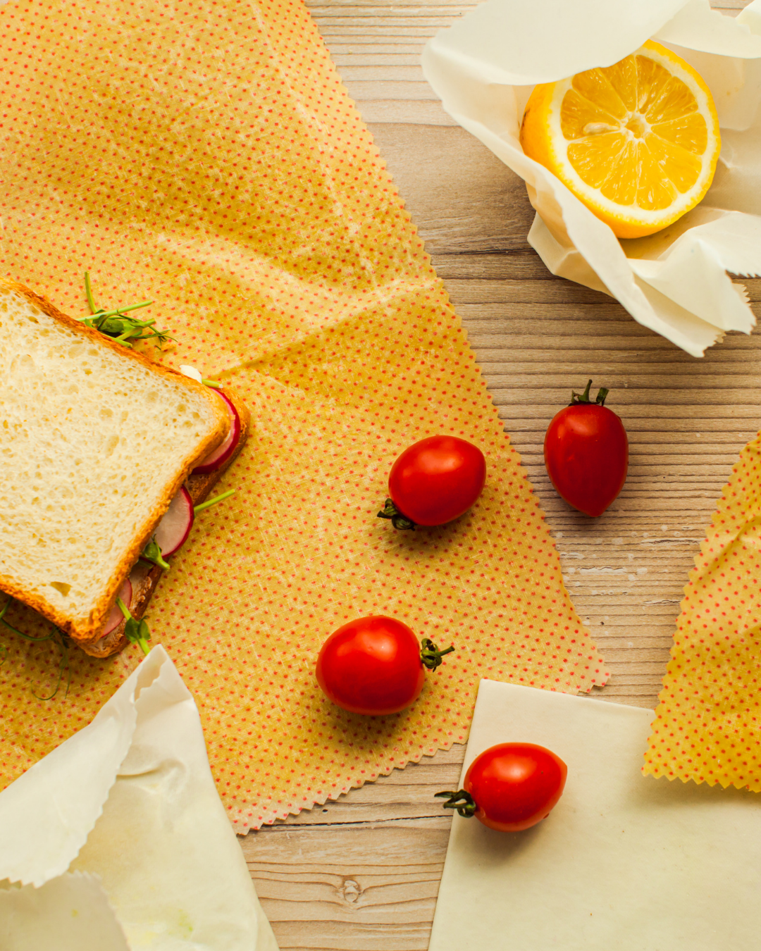 Sandwich on yellow beeswax wrap with tomatoes and lemon slices on a wooden surface