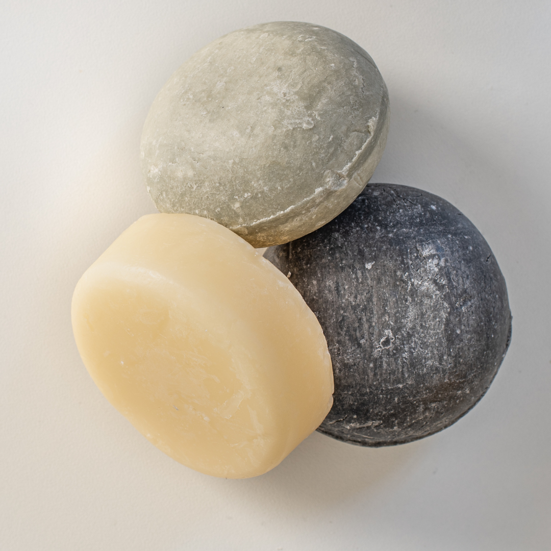 Three eco friendly shampoo bars in beige, gray, and black on a light gray background