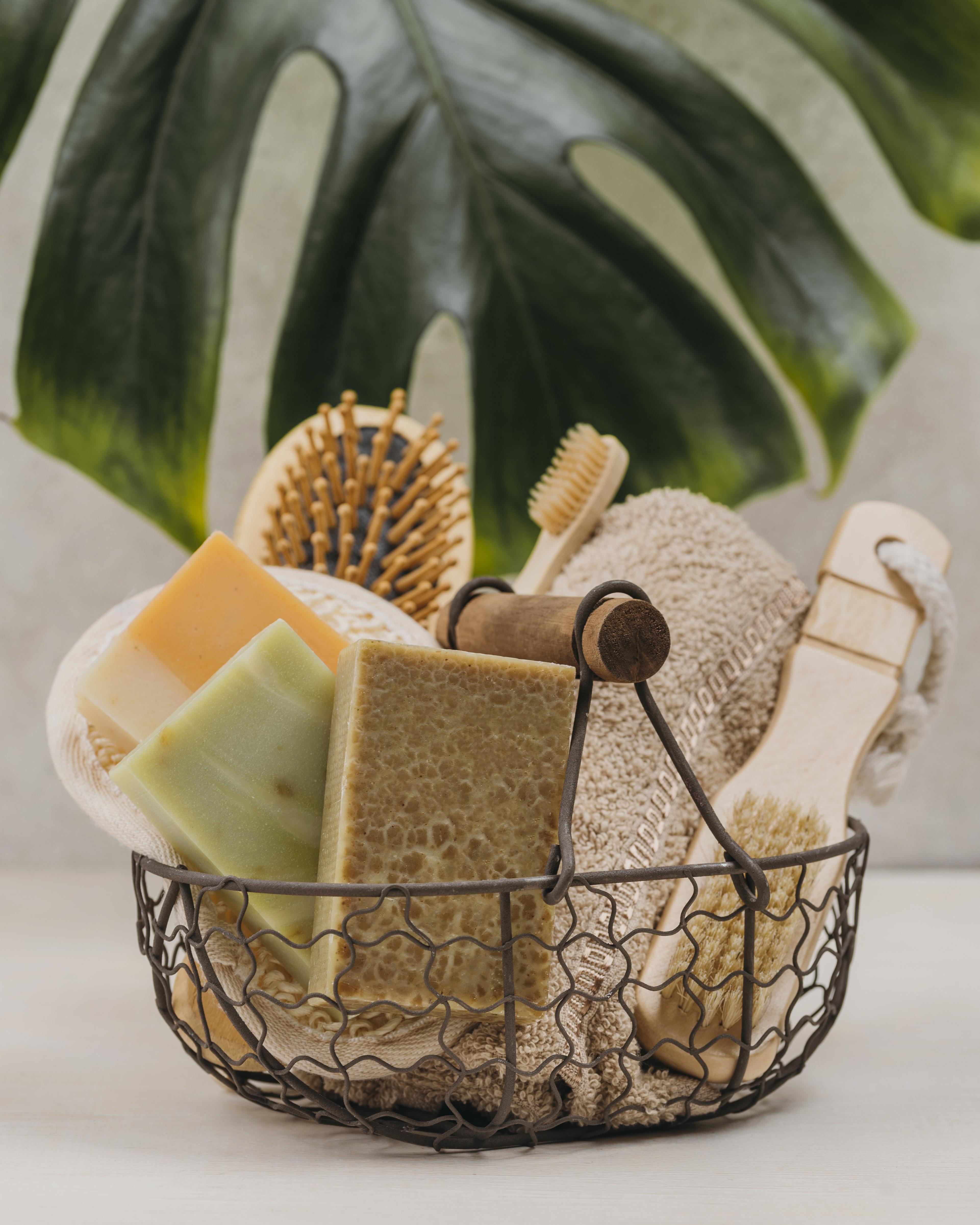 Basket with eco-friendly bath items including soap, scrubber, and brush against a leafy green background