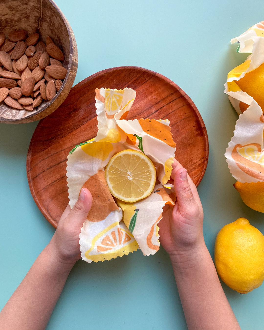 Hands holding a beeswax wrap with lemon slices on a light blue background