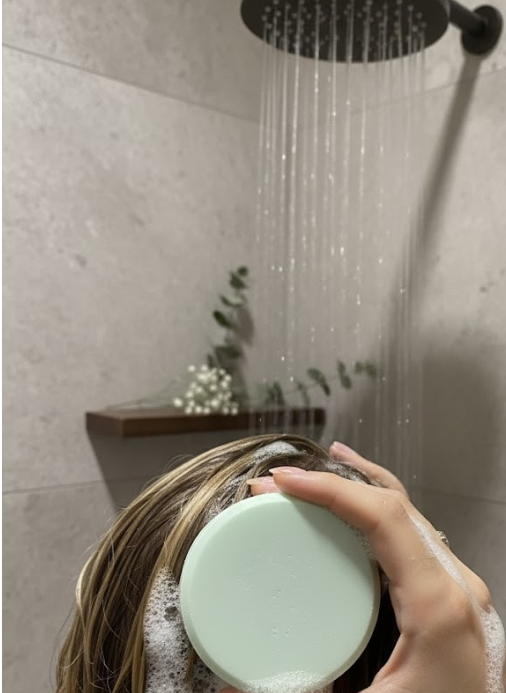 Person using a green Eucalyptus and Mint Shampoo Bar to cover their hair in a shower setting.